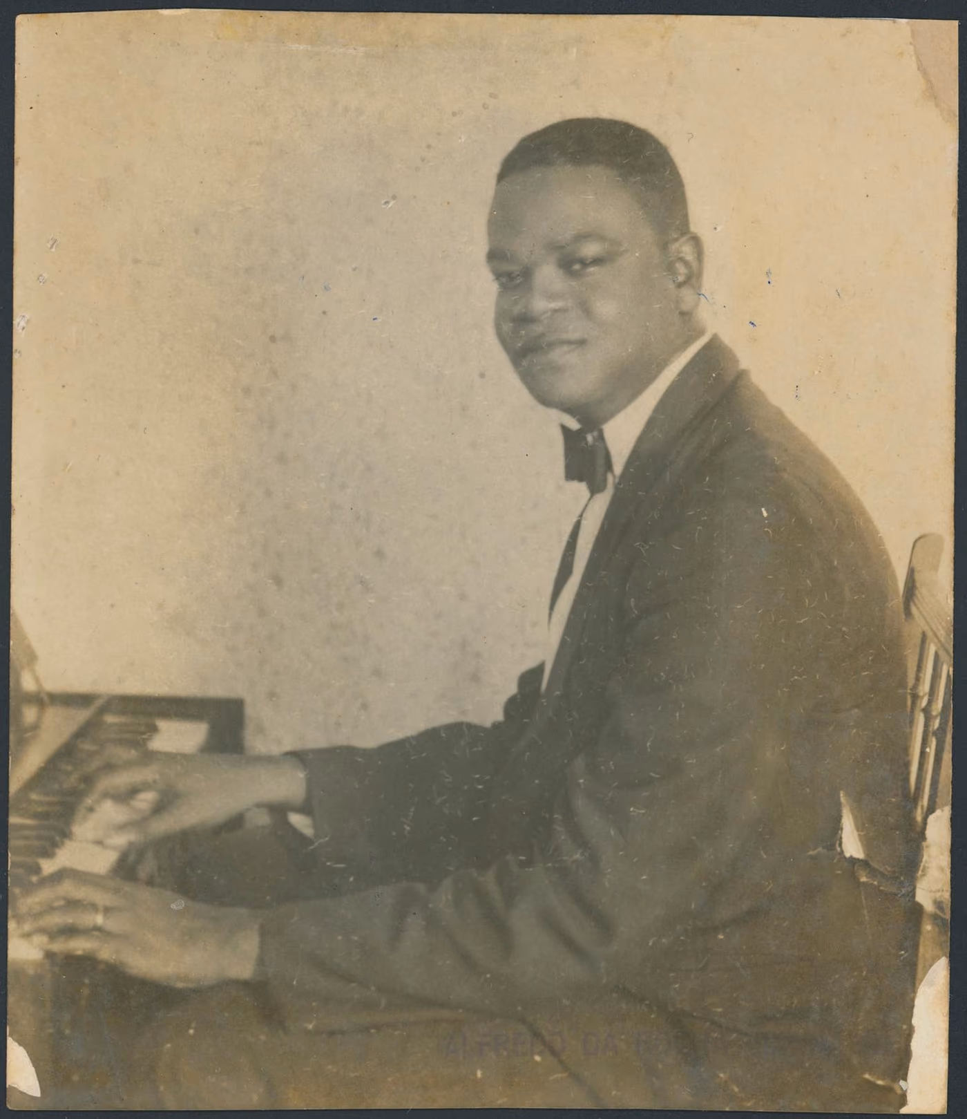 Pixinguinha, jovem, sentado ao harmônio, em fotografia de 1922.